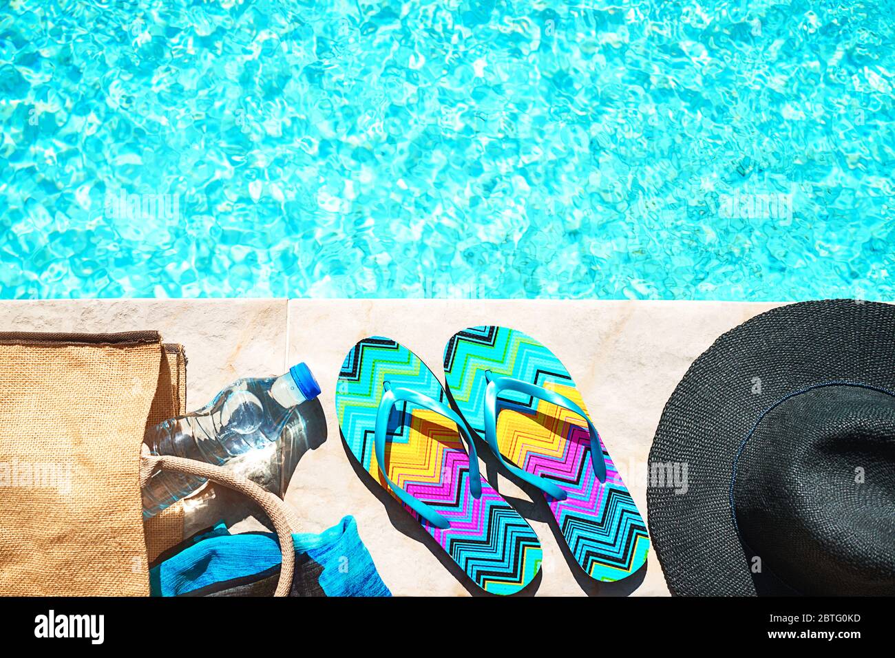 Schwimmbad und Strohhut, bunte Flip-Flops, Korb Tasche, Stroh Hut, Flasche mit Wasser als sonnigen Sommer Hintergrund. Reisen Urlaub suntan Ferienhäuser Konzept. Flach, Ansicht von oben, aus der Nähe. Stockfoto