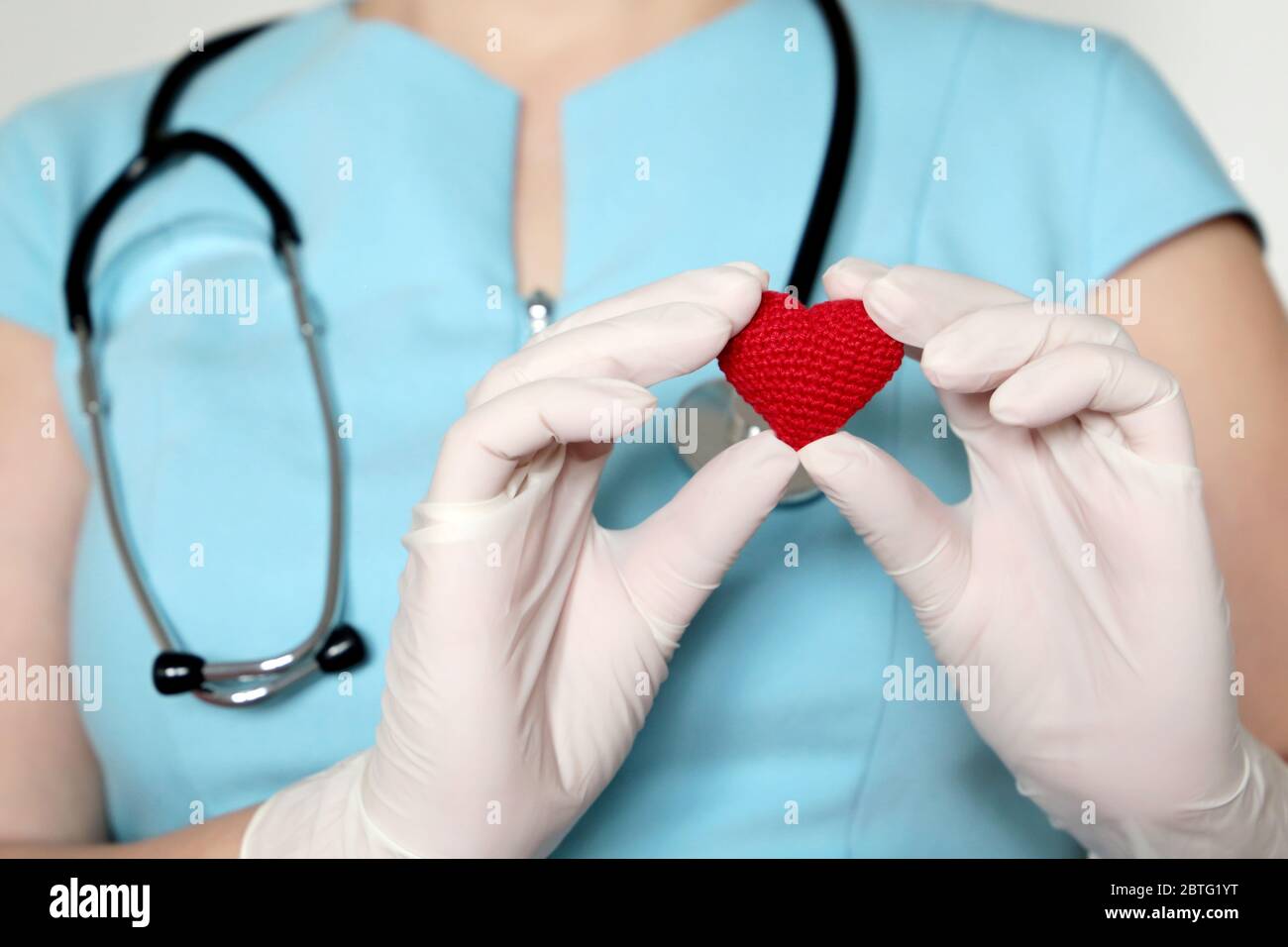Frau Ärztin in medizinischer Maske, die rotes Strickherz in den Händen hält und während einer COVID-19-Coronavirus-Pandemie Leben rettet. Kardiologe, Blutspender Stockfoto