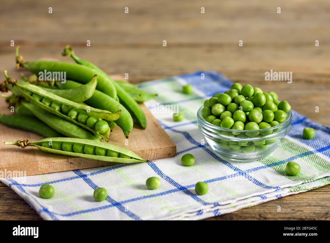 Frische grüne Erbsen in einer Glasschüssel und Erbsen in Schoten auf einem Küchentuch. Stockfoto