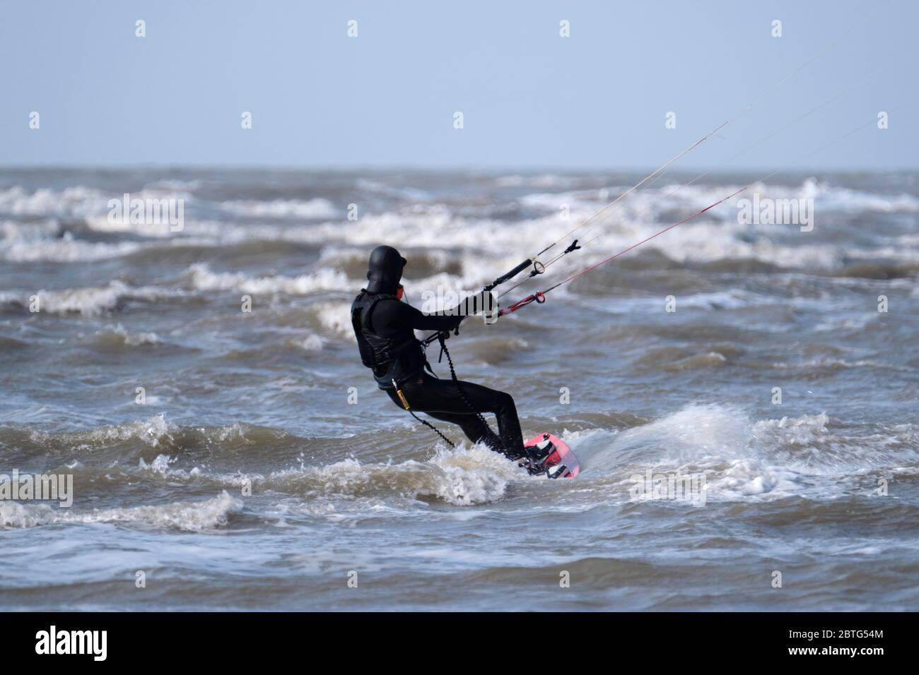 Kitesurfer in schwarzer Ausrüstung, die an einem windigen Tag auf dem Meer auf den rauen Wellen reiten Stockfoto