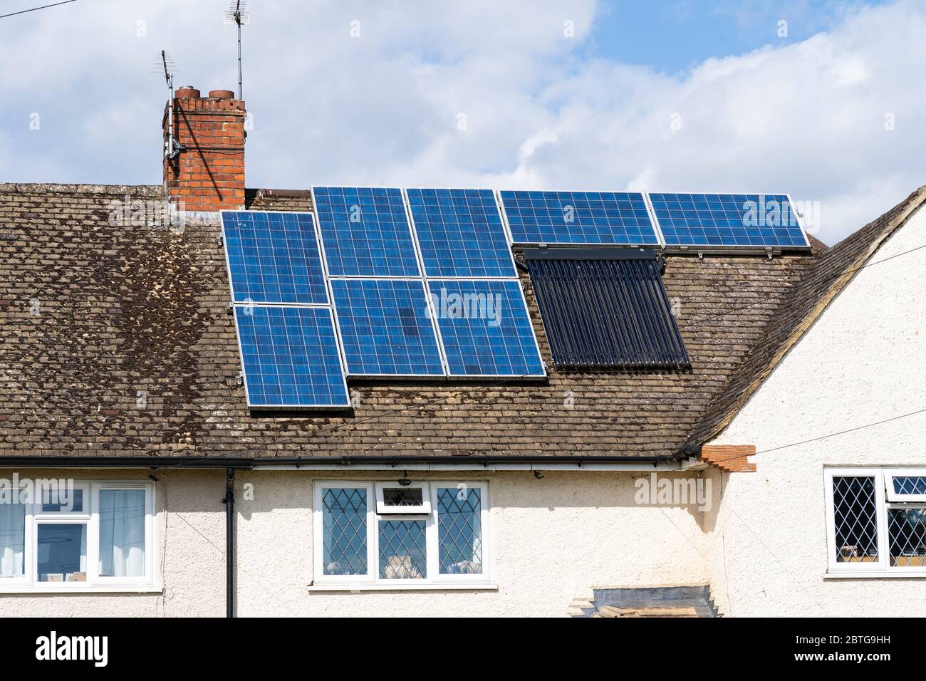Module aus Solarstromanscharen (Photovoltaik - PV) und Solarwasserwärmern, die die Sonnenenergie auf einem Hausdach in Berkshire, Großbritannien, erfassen Stockfoto