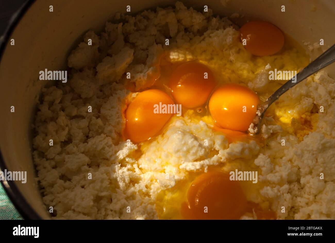 Käsekuchen kochen. Im Gefäß ist Käse und Eier geschlagen. Sonnenlicht fällt auf das Eigelb, der Rest im Schatten. Draufsicht, Stockfoto