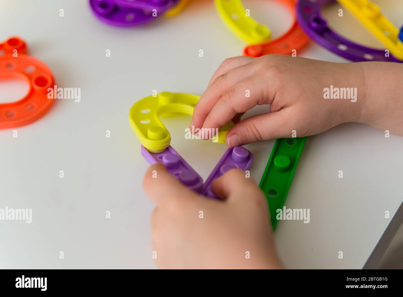 Nahaufnahme von Kind Hände spielen helle Kunststoff Spielzeug Konstruktor. Kreative Baby neue Formen. Copy Raum Stockfoto