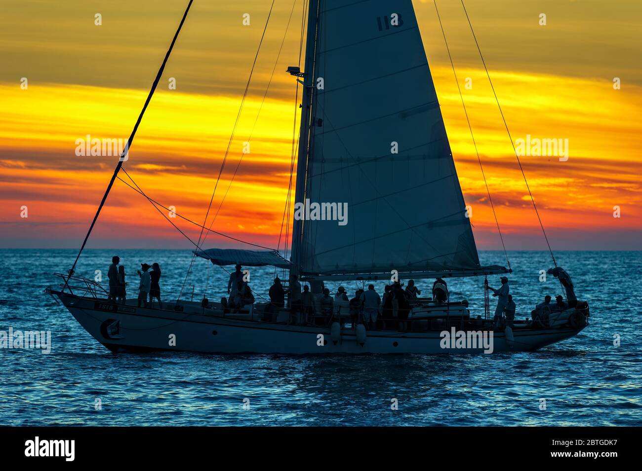 Ein Segelboot ist voll von Menschen, die eine Party am Meer bei Sonnenuntergang Stockfoto