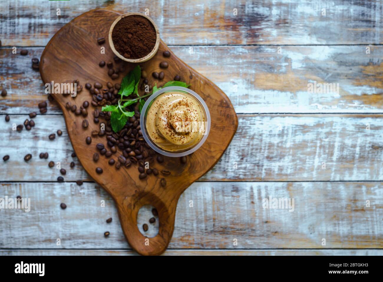 Dalgona Kaffee wird auf einem Schneidebrett mit Kaffeebohne Ornamenten serviert und von oben fotografiert. Stockfoto