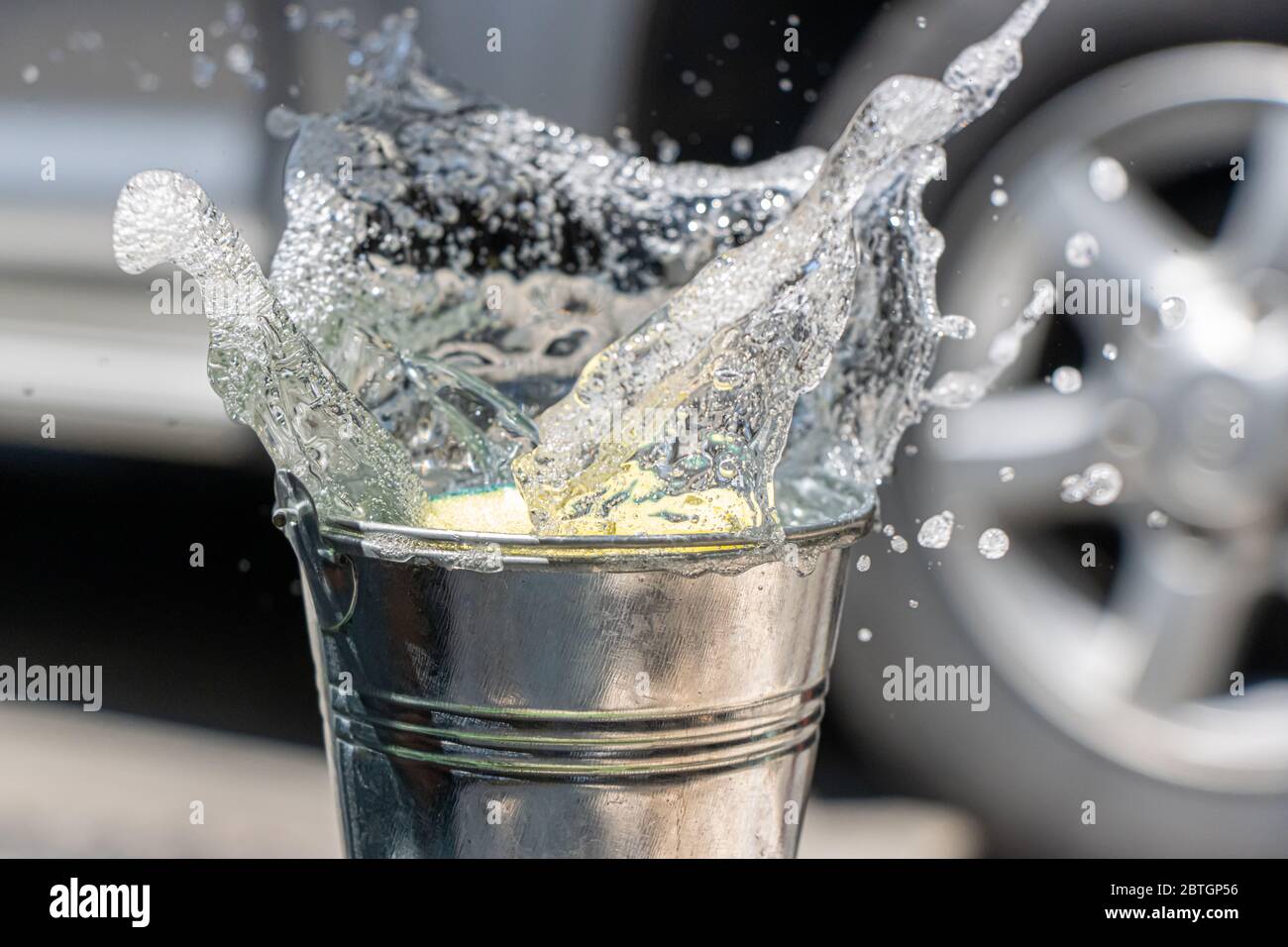 Ein Schwamm fällt mit einem Spritzer Waschmittel in den Eimer. Händewasch mit Seifenwasser. Stockfoto