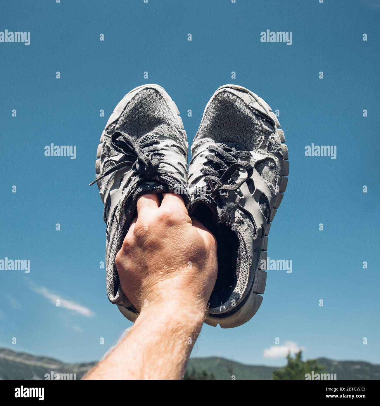 Mann hält alte Laufschuhe in der Hand auf Hintergrund bBue Himmel und Berge Stockfoto