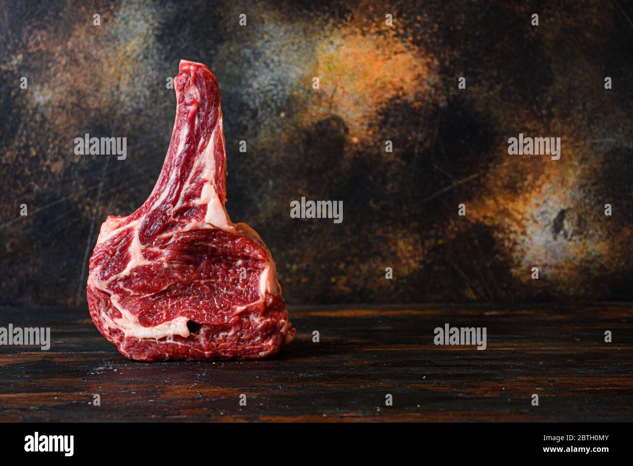 Rohes Cowboy Rindfleisch marmoriertes Steak in Metzgerei Seitenansicht über rustikalen alten Schneidebrett mit dunklen Brettern. Platz für Text. Stockfoto