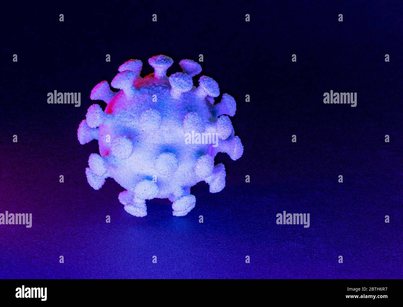 Ein bunt beleuchtetes symbolisches Virus im dunklen Rücken Stockfoto