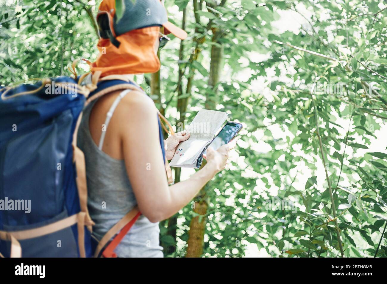 Frau, die beim Trekking eine Karte und ein Mobiltelefon auf Papier konsultiert. Stockfoto