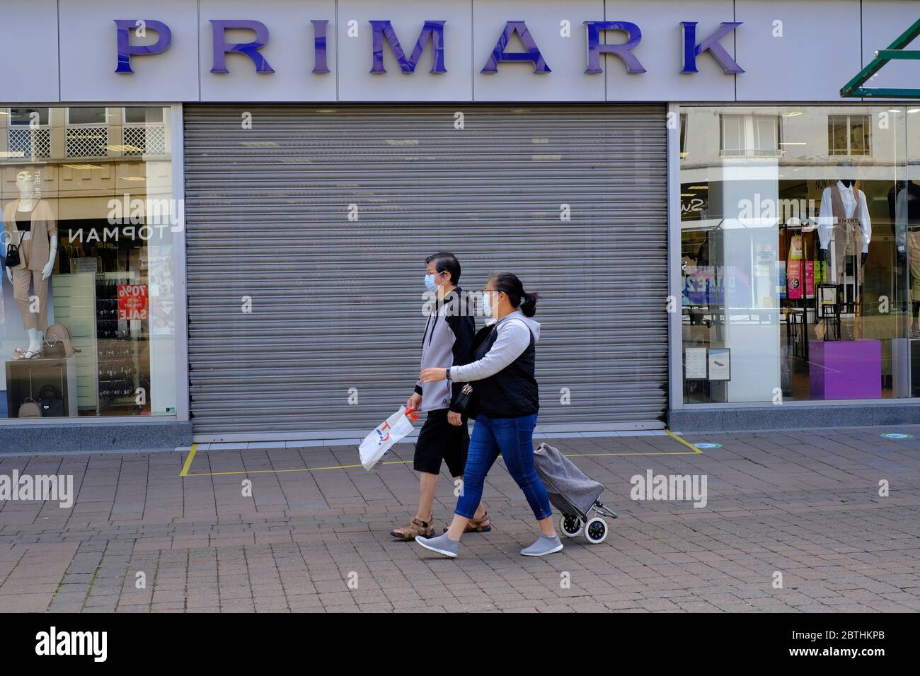 Loughborough, Leicestershire, Großbritannien. Mai 2020. Ein maskiertes Paar geht an einem geschlossenen Primark-Laden mit sozialen Distanzmarkierungen vorbei, nachdem Boris Johnson angekündigt hatte, dass nicht-essentielle Einzelhändler in England ab dem 15. Juni während der Sperrung der Coronavirus-Pandemie wieder eröffnet werden können. Credit Darren Staples/Alamy Live News. Stockfoto