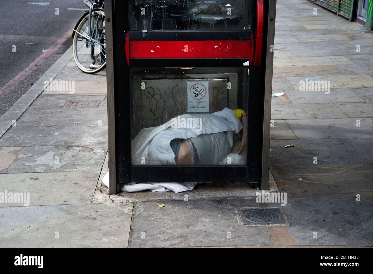 London Mai 2020 die Covid-19-Pandemie. Kingsland Road, Hackney. Obdachlose Person, die in einer Telefonbox schläft. Stockfoto