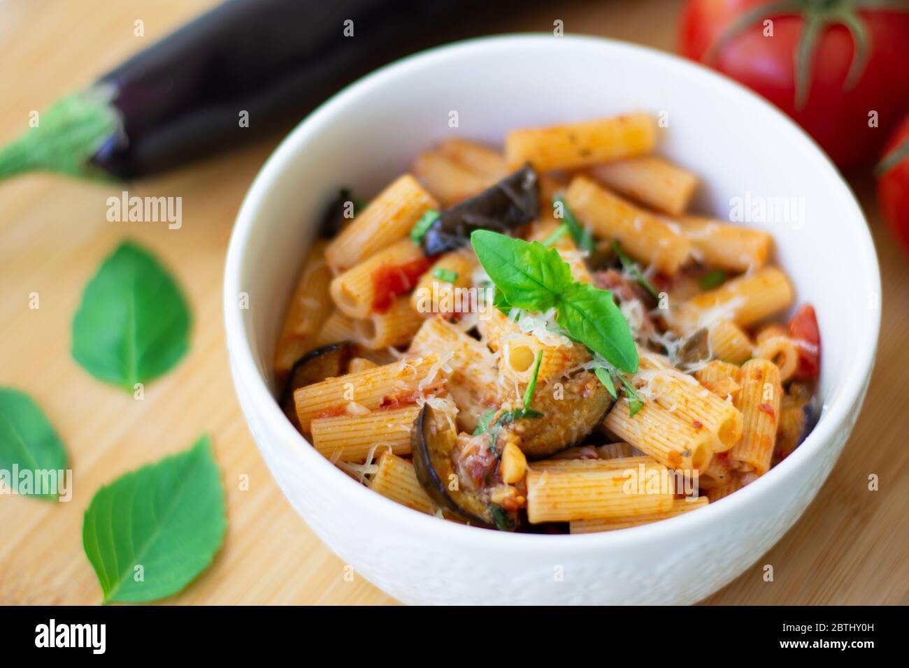 Traditionelles italienisches Gericht: Pasta alla norma mit Tomaten, Auberginen, Knoblauch, Basilikum und Ricotta auf einem Holzbrett Stockfoto