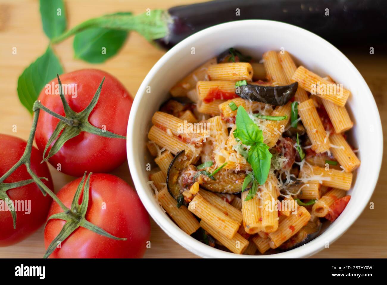 Traditionelles italienisches Gericht: Pasta alla norma mit Tomaten, Auberginen, Knoblauch, Basilikum und Ricotta auf einem Holzbrett Stockfoto