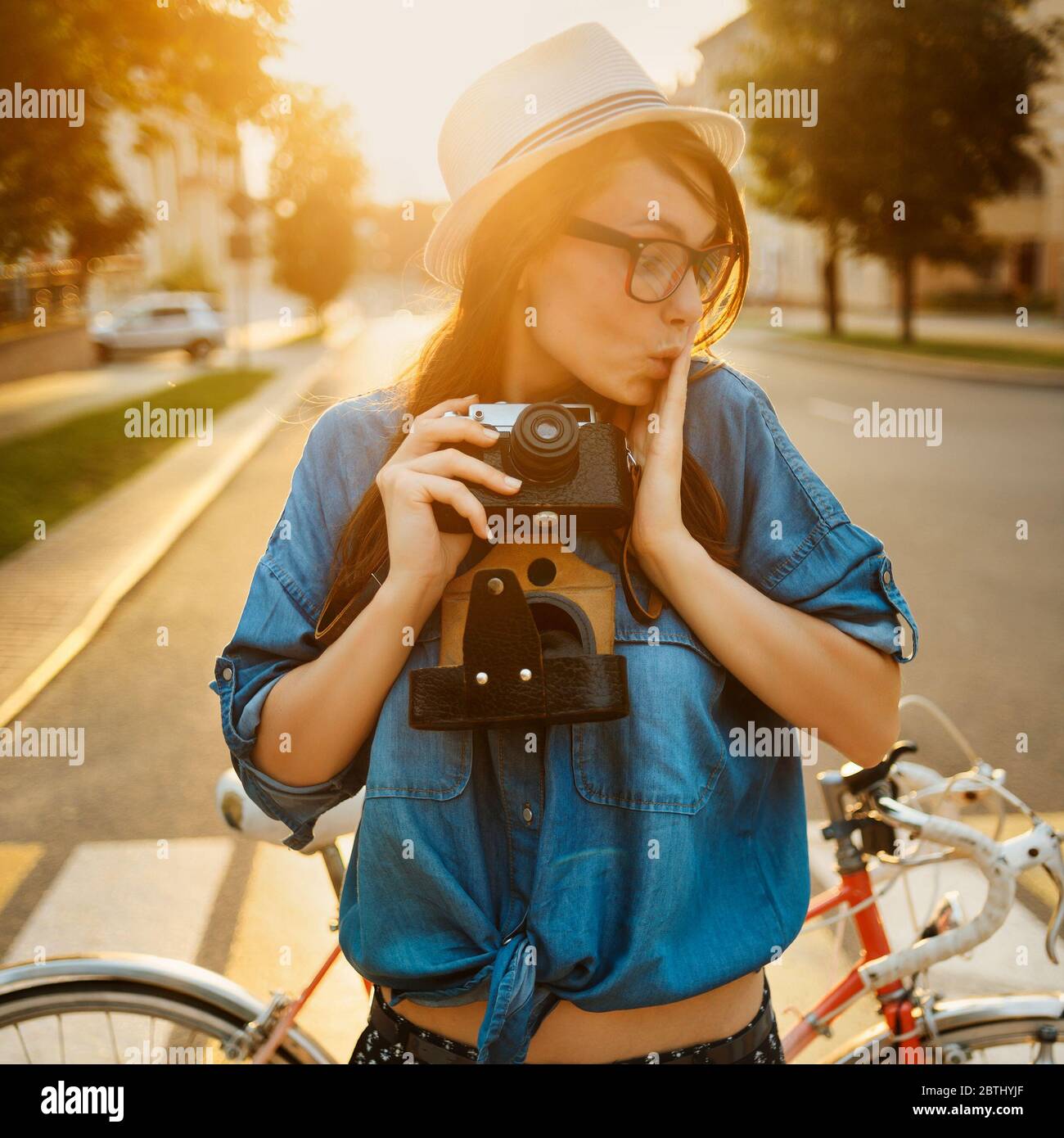 Stilvolle Frau in Hut in der Nähe Fahrrad in Morgensonne mit Foto-Kamera im Freien stehen Stockfoto