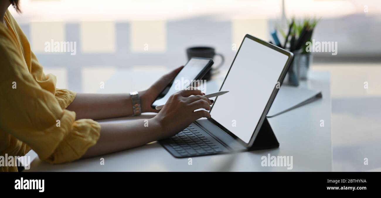 Foto von stilvollen Frau mit einem Smartphone und Stift in den Händen während vor ihrem Computer-Tablet mit Tastatur-Fall, die auf whit setzen sitzen Stockfoto