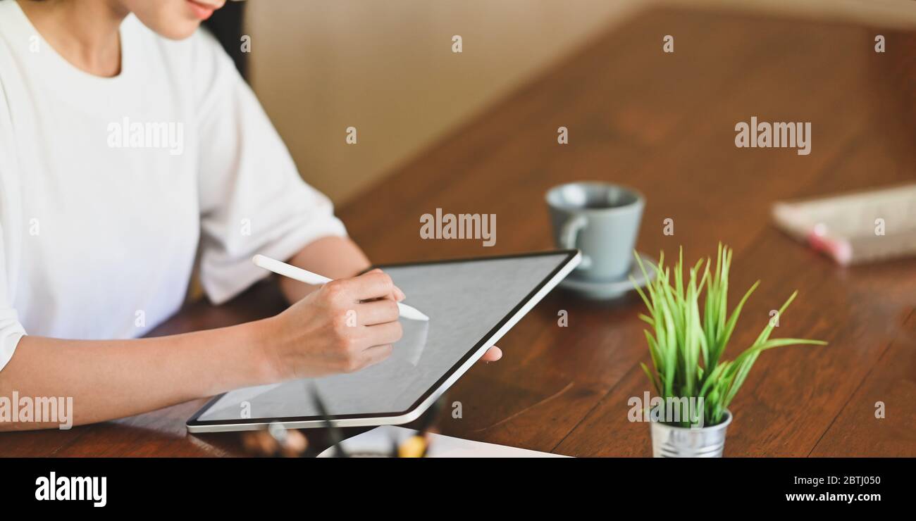 Zugeschnittenes Bild von ruhigen Frau Zeichnung auf weißen leeren Bildschirm Computer-Laptop mit Stift, während am hölzernen Schreibtisch über geordneten Sitti sitzen Stockfoto