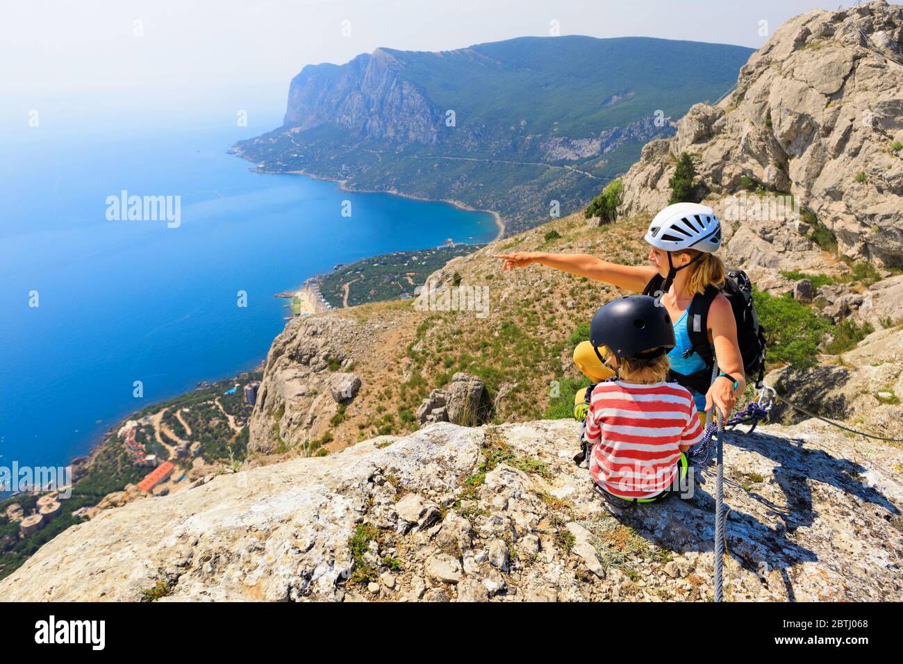 Kind, junge Mutter sitzen auf dem Gipfel. Sehen Sie sich die atemberaubende Meereslandschaft an. Familienreise Abenteuer, Wanderaktivität. Klettersteig mit Kindern. Stockfoto