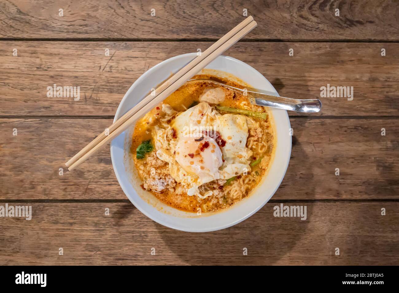 Draufsicht auf Tom Yum Nudeln mit gehacktem Schweinefleisch und Spiegelei auf Holztisch Stockfoto