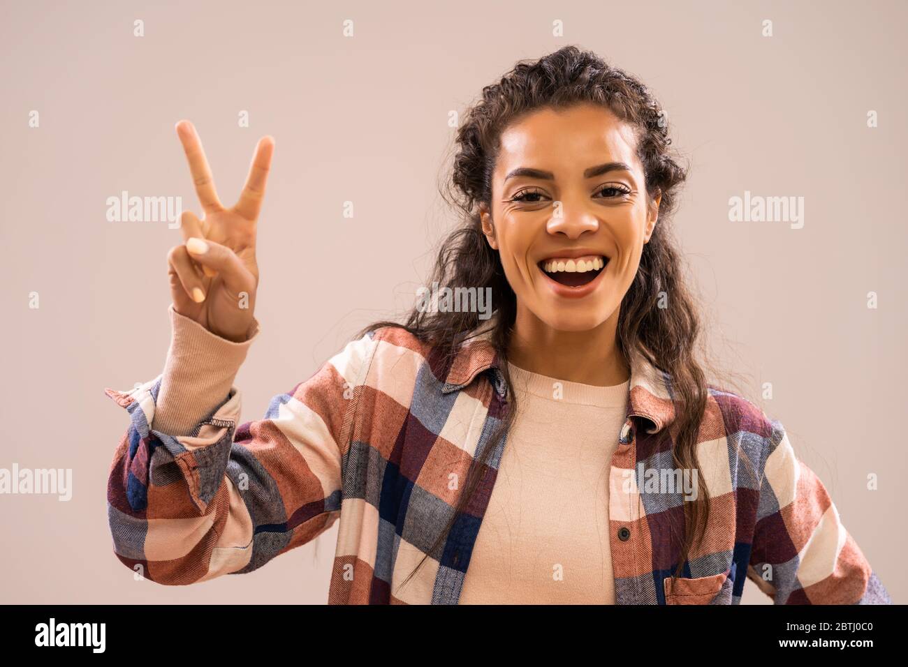 Studio-Aufnahme Porträt der schönen glücklich afroamerikanischen Ethnizität Frau in Freizeitkleidung zeigt Sieg Hand Zeichen. Stockfoto