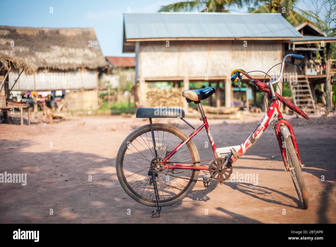 Ein rotes Fahrrad mit rotem Regenschirm in einem kleinen Dorf, Nord-Laos, Südostasien geparkt Stockfoto