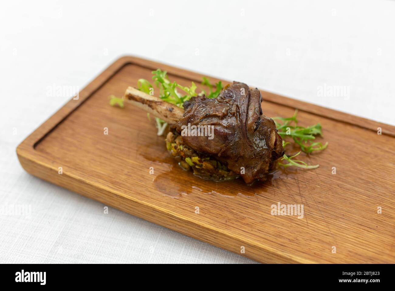 Geröstetes Fleischbein gebackenes Ganzes liegt mit frischem Tomatengemüse und heißem Pfeffer auf einer Platte auf einer alten Holzfläche Stockfoto