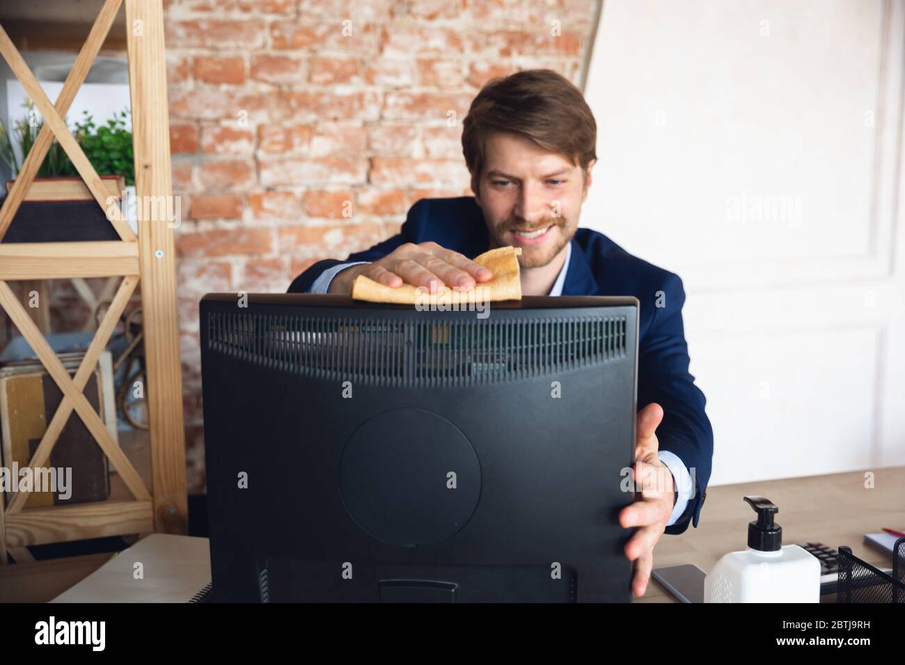 Reinigung des Arbeitsplatzes vor dem Start. Der junge Mann, Manager, kehrt nach der Quarantäne in sein Büro zurück, fühlt sich glücklich und inspiriert. Rückkehr zum normalen Leben. Business, Finanzen, Emotionen Konzept. Stockfoto