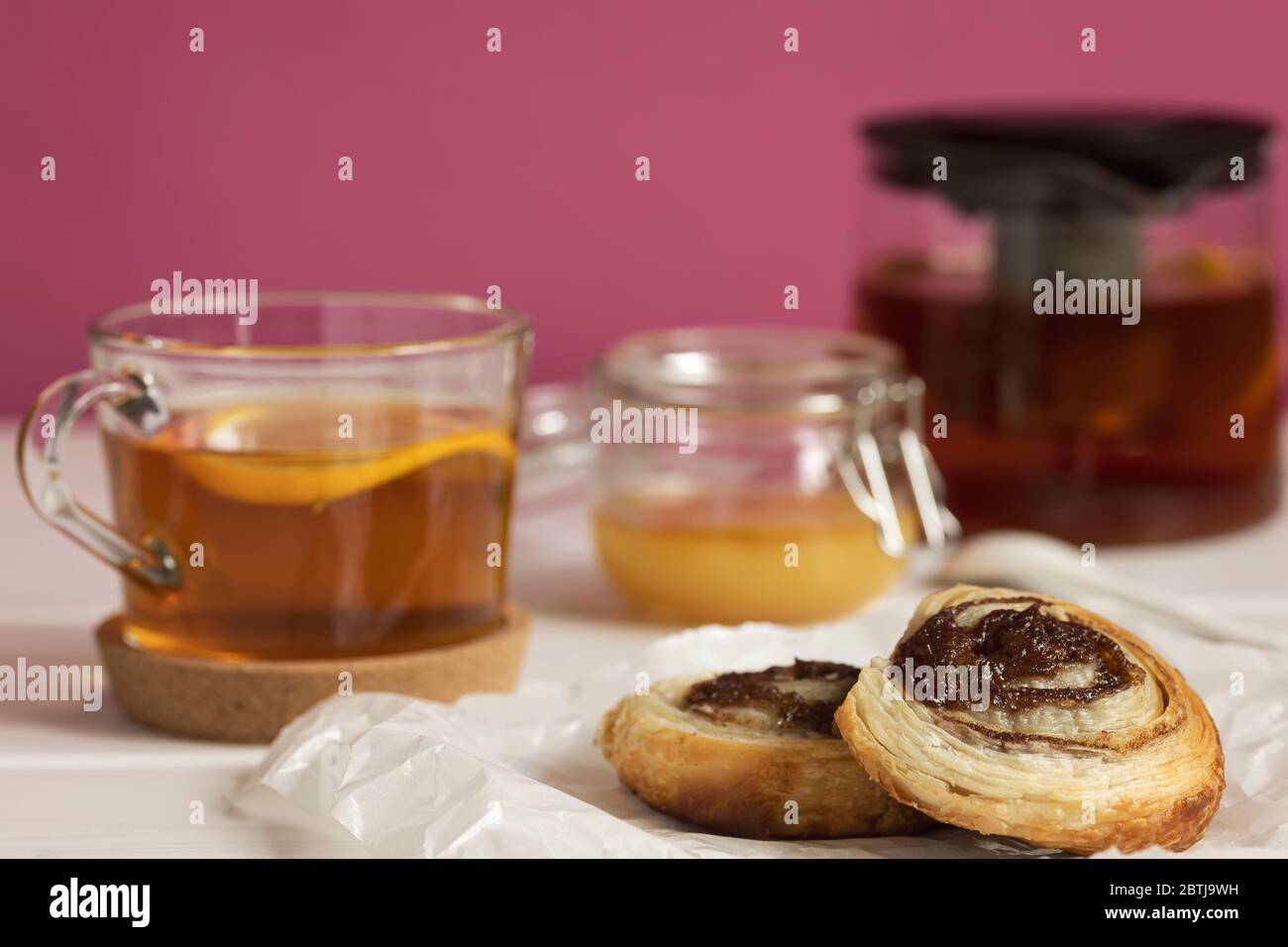 Hausgemachte Blätterteig Zimtbrötchen serviert mit schwarzem Tee mit Zitrone und Honig in einem Glas als Frühstück. Stockfoto