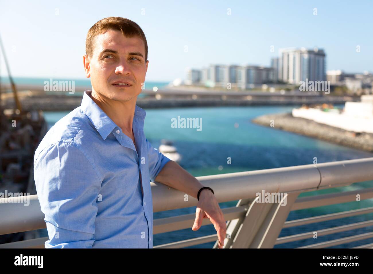 Kaukasischer Mann 30-35 Jahre alt in einem blauen Hemd auf dem Hintergrund von hohen Gebäuden Stockfoto