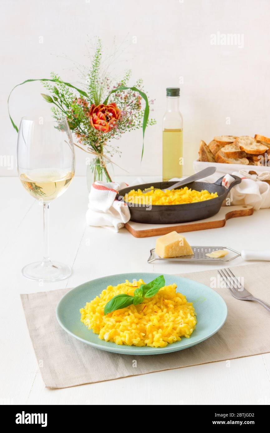Risotto Mailänder, Holztisch mit traditionellem italienischen Safranrisotto, Gläsern und Krug Wein, Flasche Olivenöl, Korb mit Brot und Blumen Stockfoto