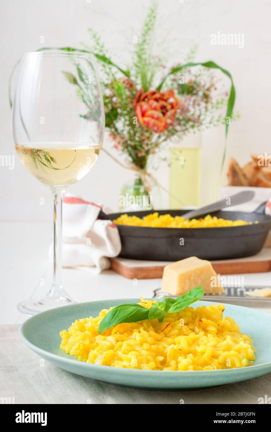 Risotto Mailänder, Holztisch mit traditionellem italienischen Safranrisotto, Gläsern und Krug Wein, Flasche Olivenöl, Korb mit Brot und Blumen Stockfoto