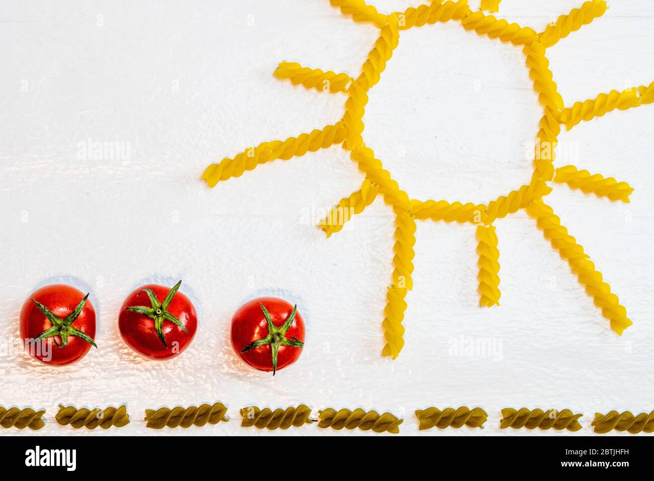 Sonne aus Fusilli Pasta, grünes Feld aus grünen Spiral-Pasta und Kirschtomaten, Konzept des Anbaus von Tomaten auf weißem Hintergrund Stockfoto