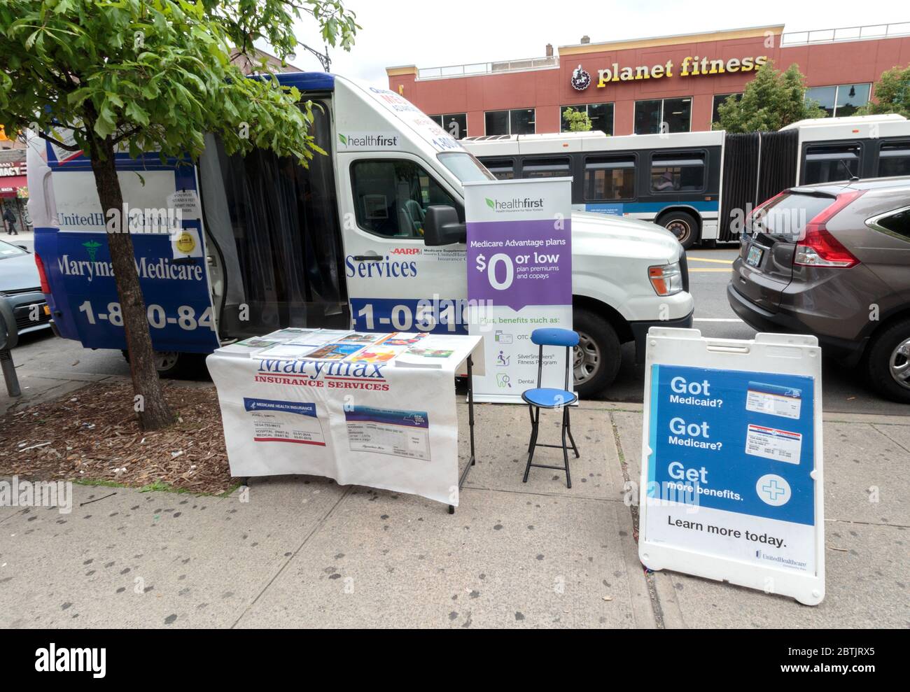 Ein geparkter Van und ein Tisch und Schilder auf dem Bürgersteig laden Passanten ein, sich für eine kostengünstige oder keine Kosten-Krankenversicherung anzumelden, ein gemeinsames Bild in Bereichen mit niedrigem Einkommen Stockfoto