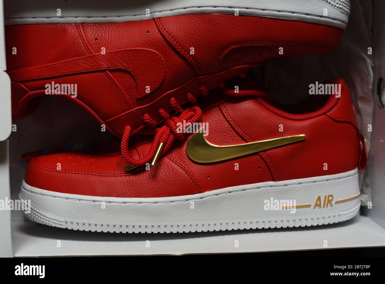 Ein sportlicher Sneaker von Nike, ein Air-Schuhmodell mit rotem Oberteil, weißer Sohle und goldenen Akzenten, darunter das berühmte Swoosh-Logo und das ti Stockfoto