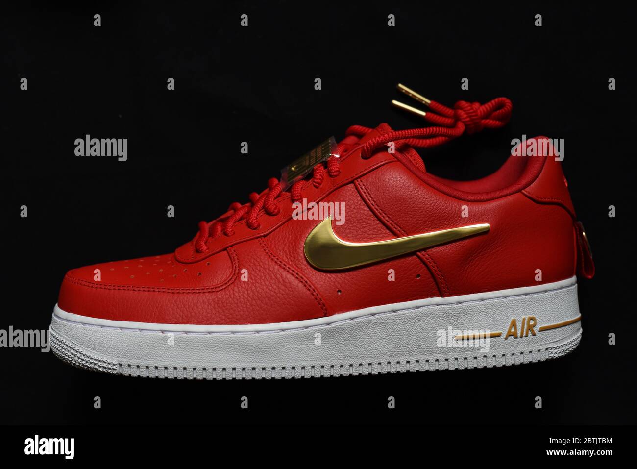 Ein sportlicher Sneaker von Nike, ein Air-Schuhmodell mit rotem Oberteil, weißer Sohle und goldenen Akzenten, darunter das berühmte Swoosh-Logo und das ti Stockfoto