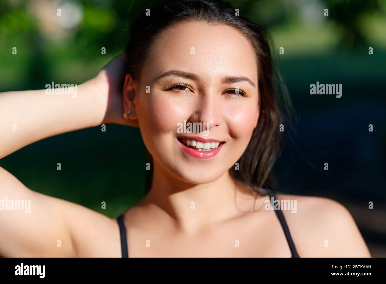 Nahaufnahme Porträt eines jungen schönen lächelnden glücklich Brünette Mädchen im Freien Park an einem sonnigen Sommertag, Korrektur der Hand lose Haare. Stockfoto