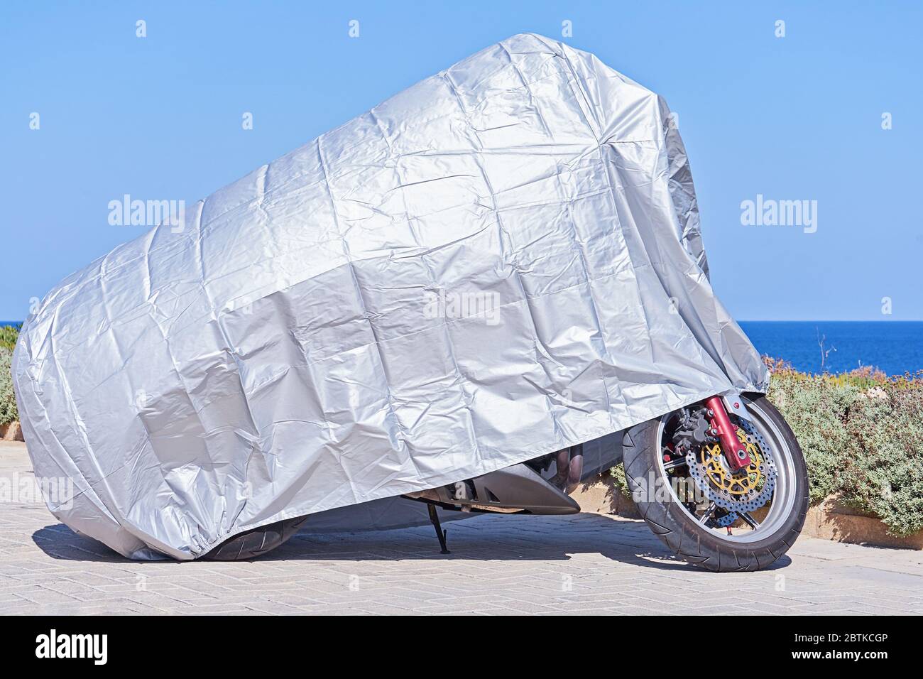 Wasserdichte Abdeckung für Motorrad mit silberner reflektierender Schutzfläche. Motorrad mit Stoffschild bedeckt, im Freien abgestellt Stockfoto