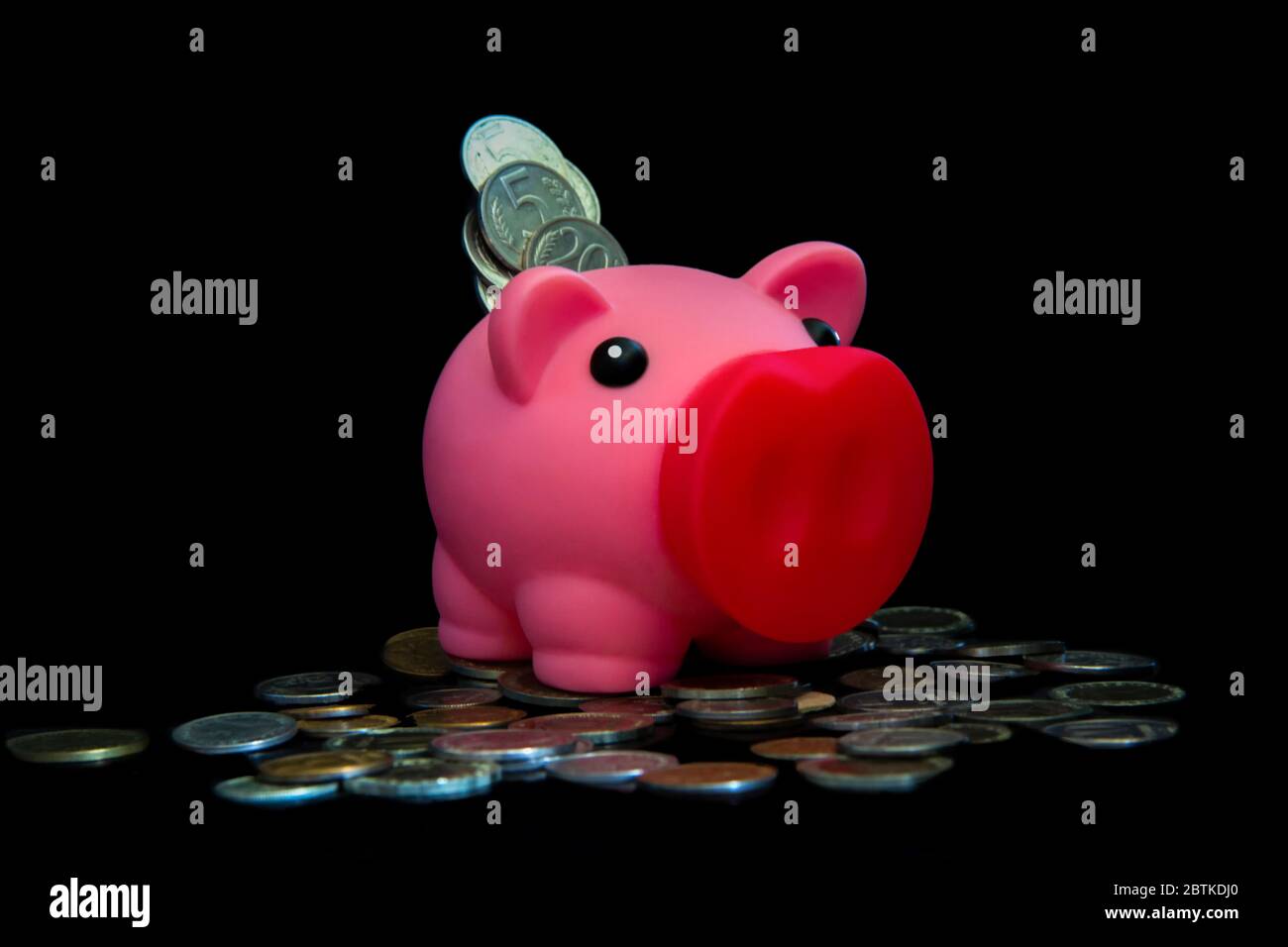 Rosa Sparschwein voller Münzen auf schwarzem Hintergrund. Konzept, wo Sie Ihre Einsparungen investieren. Geld verdienen Stockfoto