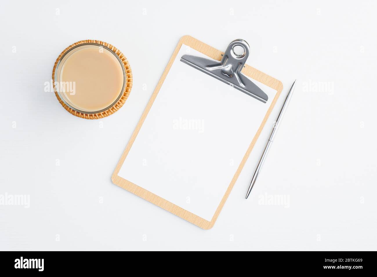 Klemmbrett mit leerer Note und Tasse Kaffee auf weißem Tisch. Flach liegend, Draufsicht. Modernes Büroschreibtischkonzept. Stockfoto