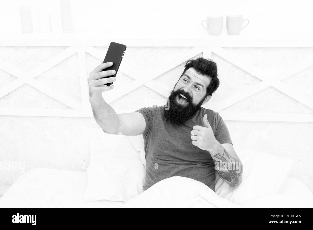 Nur Daumen hoch. Happy hipster geben Daumen bis zu Handy Kamera. Bärtiger Mann Lächeln mit Daumen hoch und Smartphone. Gestik, die Zufriedenheit. Daumen hoch für die neue Technologie. Mobilen Lebensstil. Das moderne Leben. Stockfoto