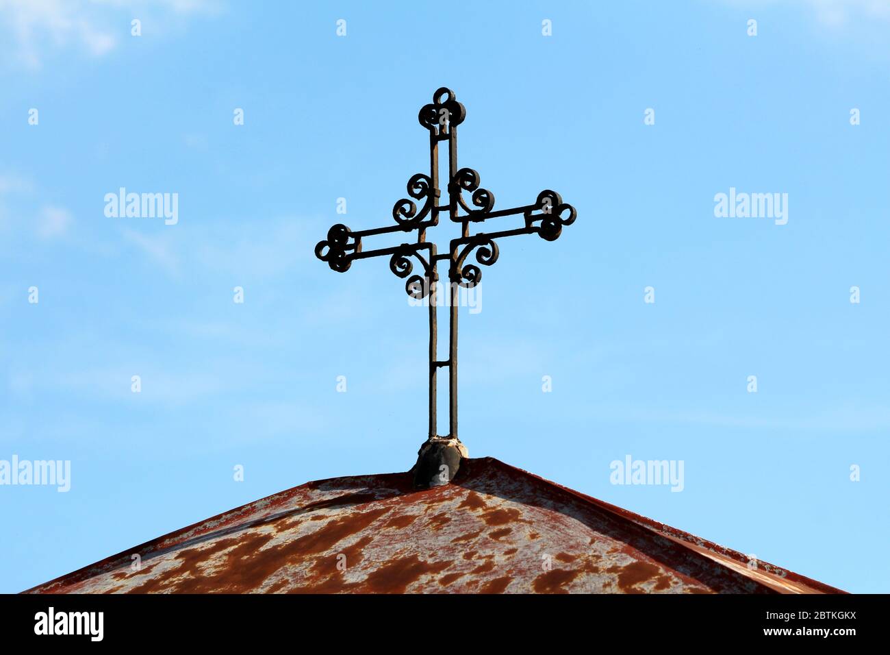 Verrostete alte antike Vintage Retro Gothic Metallkreuz mit dekorativen Elementen auf der Spitze der kleinen Kapelle mit verrosteten Blech bedeckt Dach montiert Stockfoto