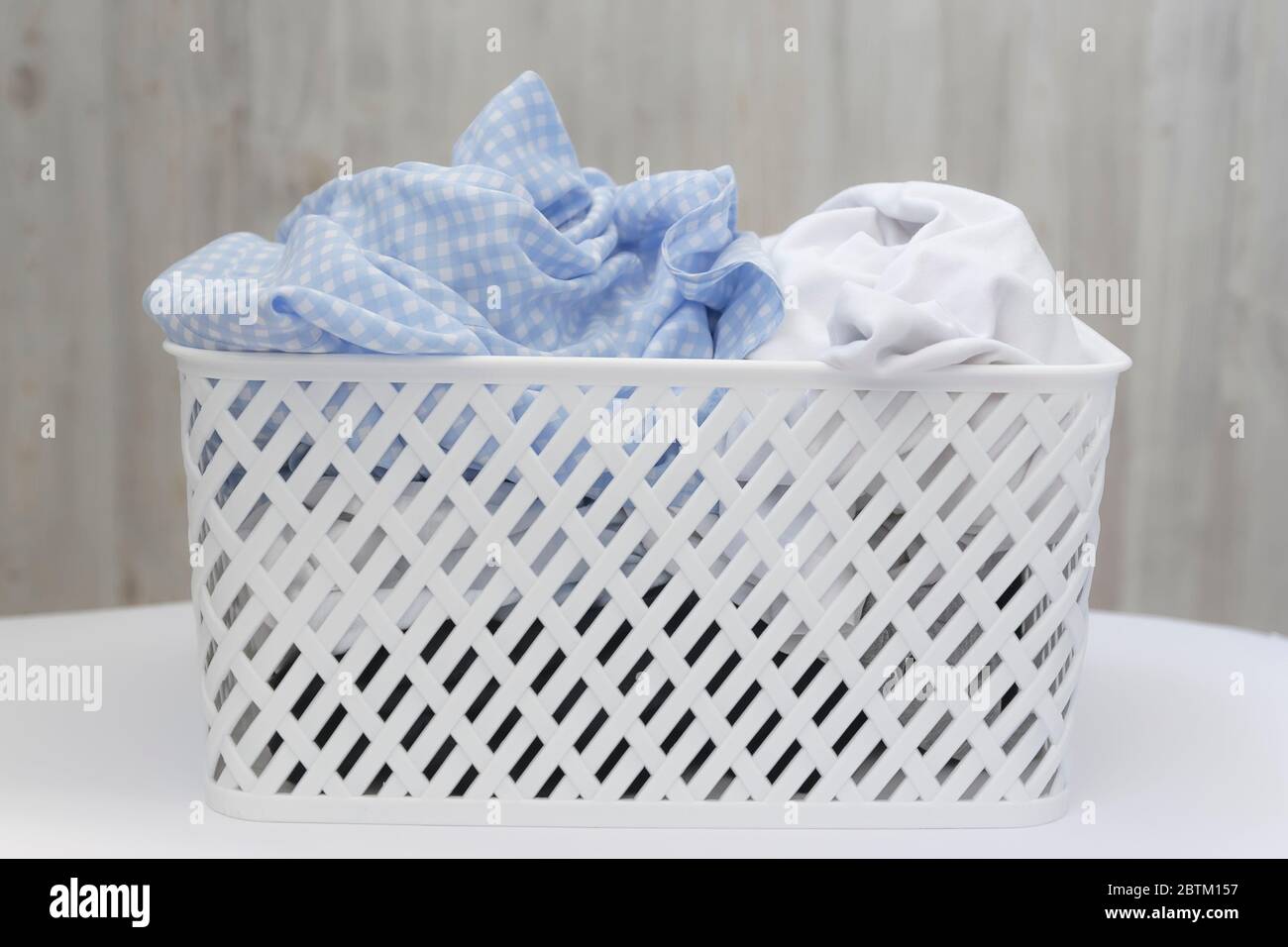 Blaue und weiße schmutzige Sachen in einem weißen Plastikwäschenkorb auf einem grauen Wandhintergrund. Waschen, Hausreinigung Stockfoto