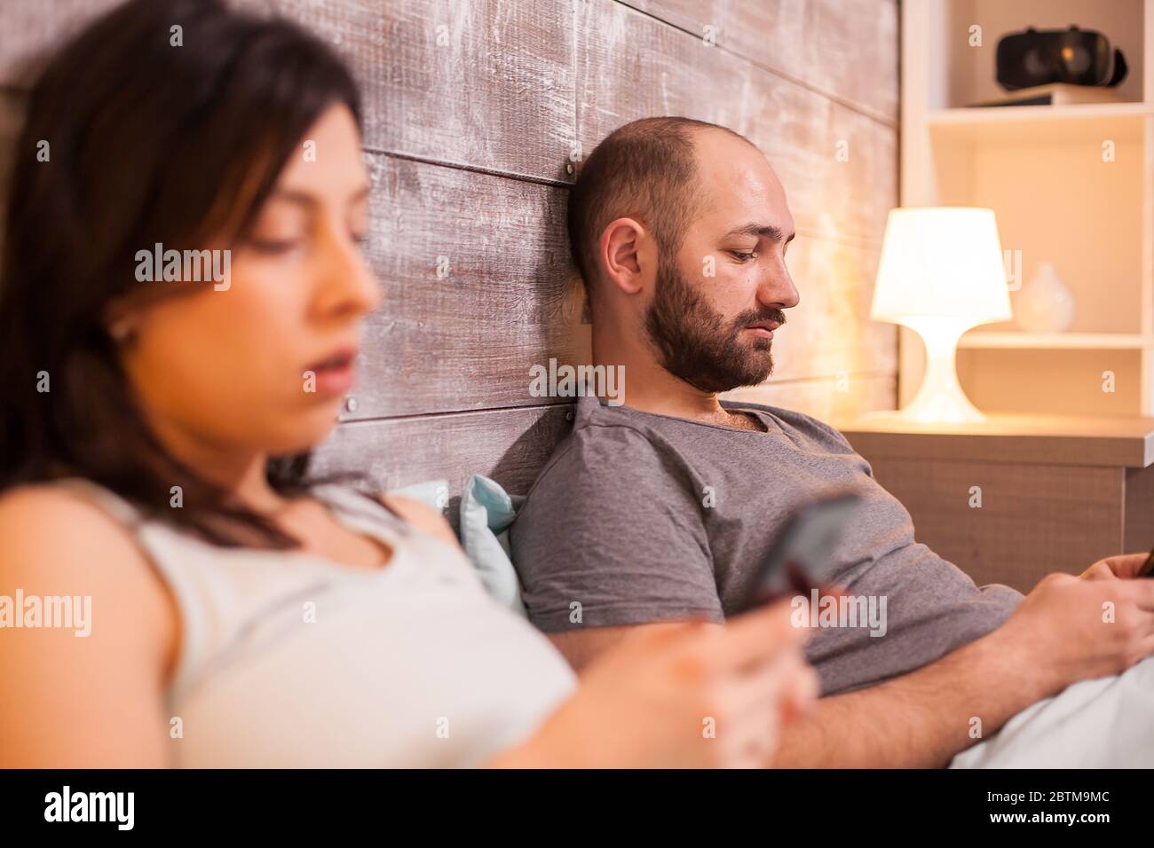 Entferntes Paar im Bett vor dem Schlafengehen mit dem Smartphone. Stockfoto