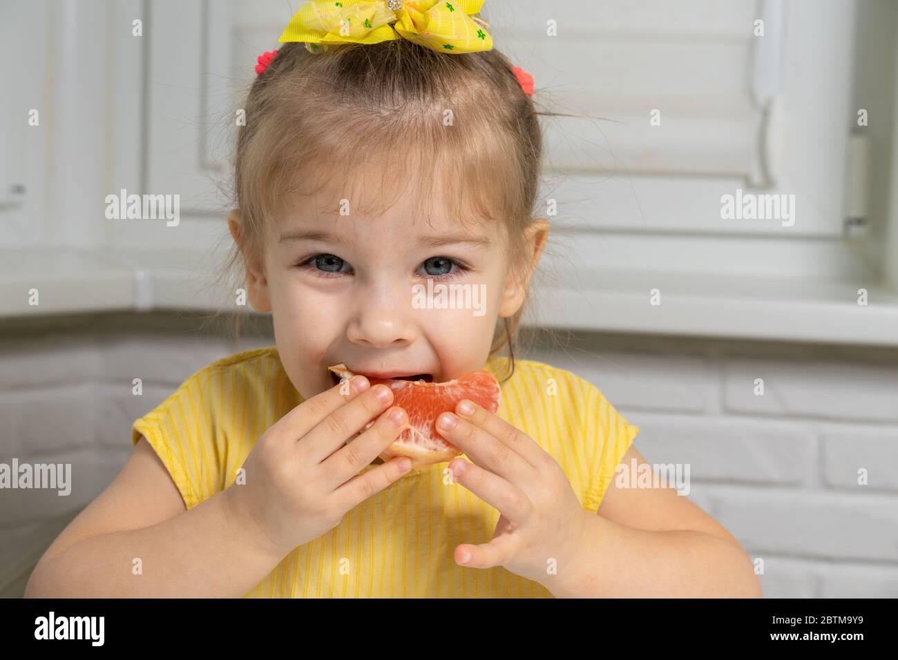 4 Jahre altes Mädchen in einer gelben Bluse isst Grapefruit Stockfoto