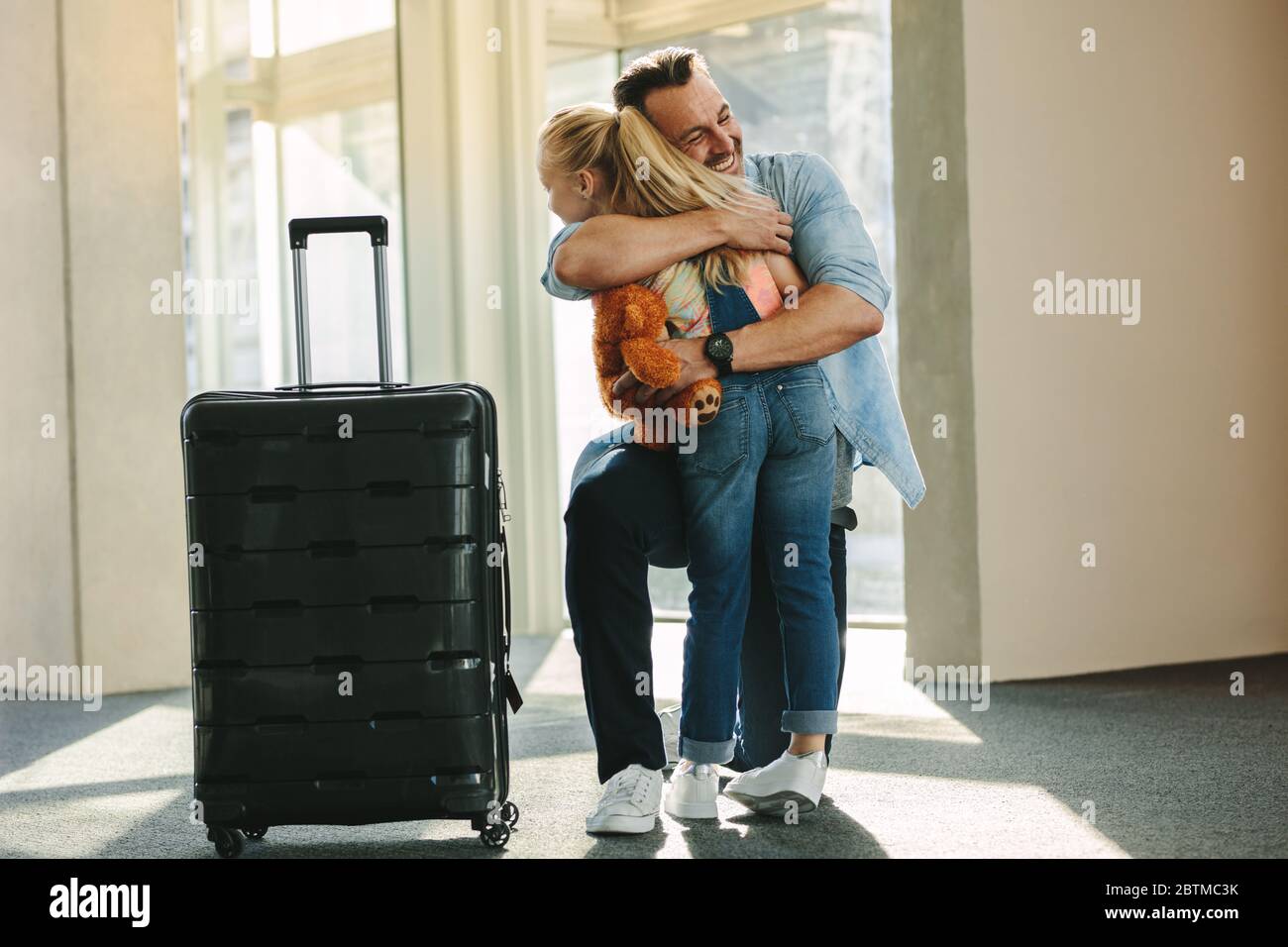 Mädchen begrüßt ihren Vater an der Tür, wenn er von einer Reise zurück kommt. Tochter umarmt ihren Vater gerade von einer Geschäftsreise mit einem Reisekoffer. Stockfoto