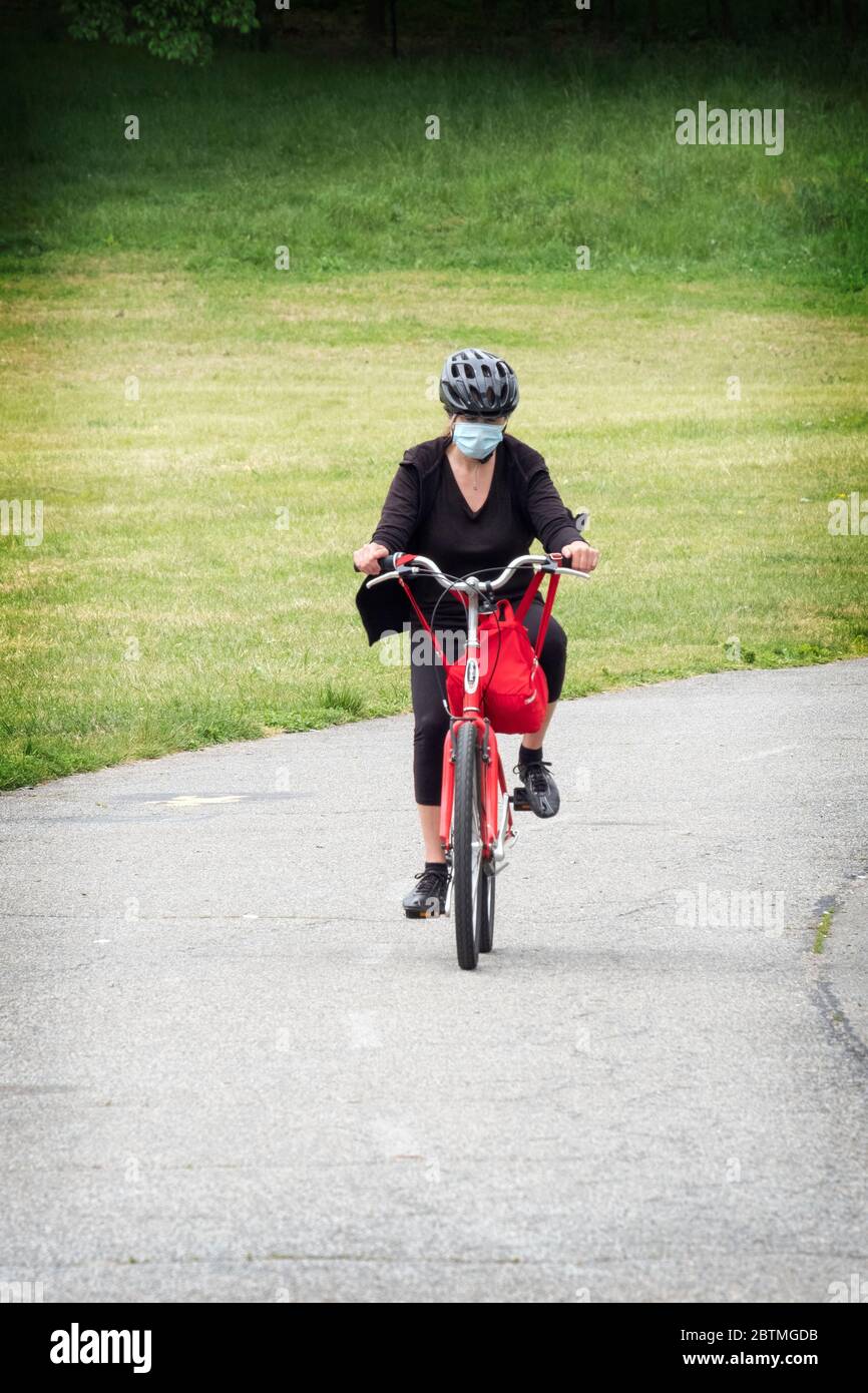 Eine Radfahrerin, die während der Coronavirus-Pest eine chirurgische Maske trägt. Reiten auf dem Weg in Little Bay Park, Whitestone, Queens, New York City Stockfoto