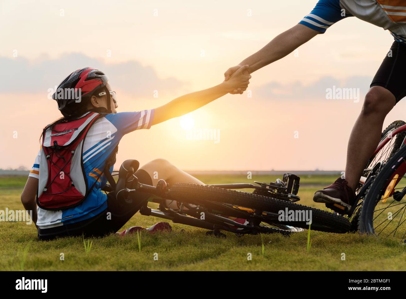 Frau Mountainbike fahren war Unfall abgestürzt und fiel auf das Gras, während ein Liebhaber ihr Kommen in die schöne Sonnenuntergang Zeit zu helfen. Verwenden von Hilfe und Stockfoto