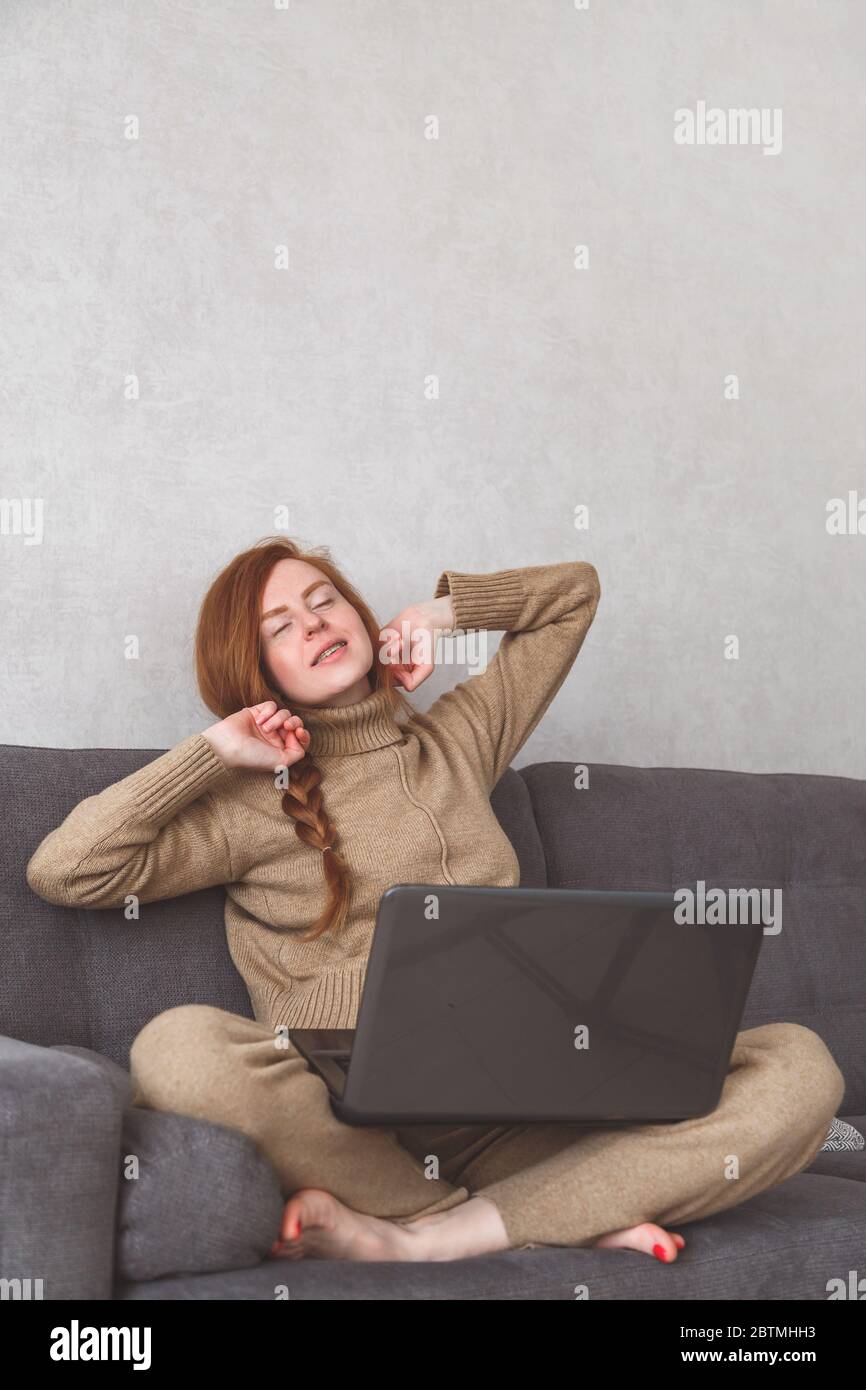 Junge Frau dehnt sich nach der Arbeit oder Online-Konferenz auf dem Sofa. Freiberuflich, zu Hause Stockfoto