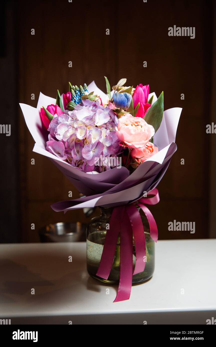 Ein großer Strauß von bunten Blumen verschiedener Art steht in einer transparenten Glasvase. Stockfoto