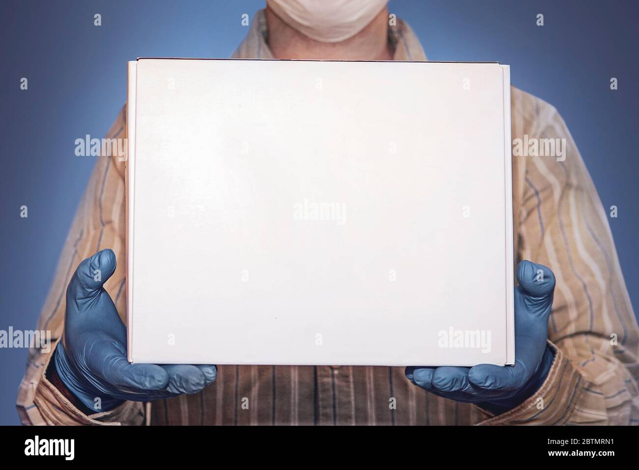 Konzept der Lieferware bei Quarantäne 2019-ncov. Junger Mann in medizinischer Maske und blauen Handschuhen hält Pappkarton in den Händen. Kontaktlose Lieferung Stockfoto